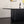A modern black ribbed pedestal dining table with a white curved tabletop, styled in a minimalist room with a wine bottle, wine glass, and vase on top.