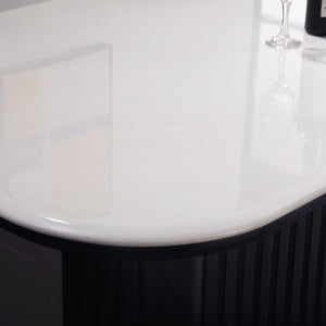 Close-up of a glossy white curved tabletop with a dark ribbed base, showing reflections and part of a wine glass on the surface.