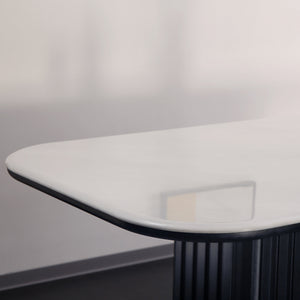 A modern white table with a glossy finish and a dark ribbed base, shown in a minimalist interior setting with a wine bottle and a glass on top.