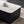 A modern rectangular coffee table with a glossy white top and a black ribbed pedestal base, styled on a textured beige rug with a coffee cup on top.