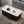 A modern rectangular coffee table with a white top and a dark ribbed base, styled on a geometric rug in a contemporary room with large windows overlooking a lake and forest.