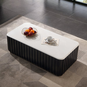 A modern rectangular coffee table with a white top and a dark ribbed base, styled on a geometric rug in a contemporary room with large windows overlooking a lake and forest.