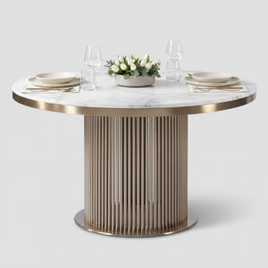 A modern round dining table featuring a white marble top with subtle gray veining and a fluted metallic pedestal base in a champagne gold finish.