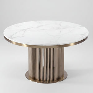 A round dining table featuring a white marble top with subtle gray veining and a fluted metallic pedestal base in a champagne gold finish.