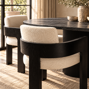 Black oval dining table with beige upholstered dining chair at corner