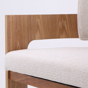 Close-up detail of a modern wooden chair with a light beige textured fabric seat cushion and a natural wood frame against a white background.