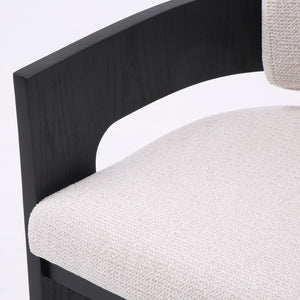 Close-up of a modern chair showing a curved black wooden frame and a light beige textured fabric seat cushion against a plain white background.