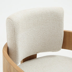 Close-up of a modern chair showing a curved light beige textured fabric backrest and seat, paired with a natural oak wood frame, on a white background.