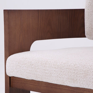Close-up of a modern armchair corner showing a dark brown wood frame and a textured off-white woven seat cushion against a white background.