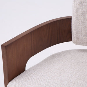Close-up of a modern armchair featuring a curved dark walnut wood frame and textured light beige fabric upholstery.
