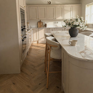 Modern kitchen with light wood cabinets, marble countertops, and pendant lights.