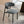 A modern gray upholstered dining chair with a curved backrest and black metal legs, shown in a bright interior setting next to a round table.