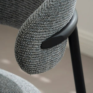 Close-up of a modern armchair with a textured gray woven fabric upholstery and a matte black metal frame.