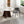 A modern round dining table with a white marble-look top and dark wood pedestal base, styled in a bright room with two upholstered chairs on a light rug.