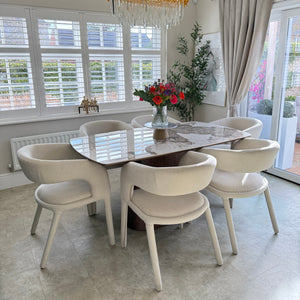 Dining room with a round marble table and four chairs, featuring a decorative chandelier and floral arrangement.