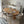 A modern dining room setup featuring a round light oak wood table surrounded by six white upholstered chairs with curved backs and light wood legs, set on a textured white rug.