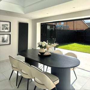 Modern dining area with a black table and white chairs, featuring a skylight and view of a garden.