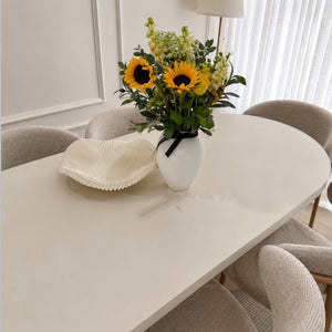 Dining table with a vase of sunflowers and white chairs in a bright room.