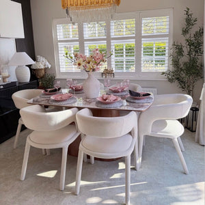 Dining room with a round table and white chairs, featuring a chandelier and decorative elements.