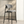 A modern bar stool with a curved gray upholstered backrest and seat on a black metal frame, shown in a minimalist interior setting with a white wall, framed abstract art, and soft natural light.