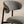 A close-up of a modern bar stool featuring a textured gray woven fabric seat and curved backrest, supported by a slim black metal frame against a plain beige wall.