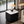 A modern square side table with a black pleated base and a white marble top, styled in a contemporary living room with a table lamp on top.