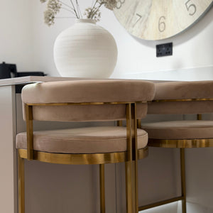Beige chairs with gold legs in a room with a clock and vase on the wall.