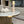 A round coffee table with a white marble top and fluted gold base, styled with a wooden candlestick holder and a decorative bowl of white decorative balls in a modern living room setting.
