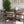 A modern dining room scene featuring a dark wood oval table surrounded by six upholstered dining chairs with curved backs and wooden frames. A large green potted plant stands in the corner, and two framed abstract prints hang on the wall above the table.