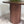 A modern oval wooden dining table with a fluted cylindrical pedestal base, shown in a styled interior setting with a green plant and patterned rug.