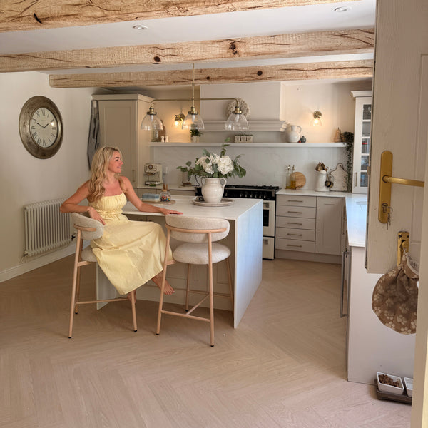 Woman in a yellow dress standing in a small kitchen with white cabinets and a white countertop.